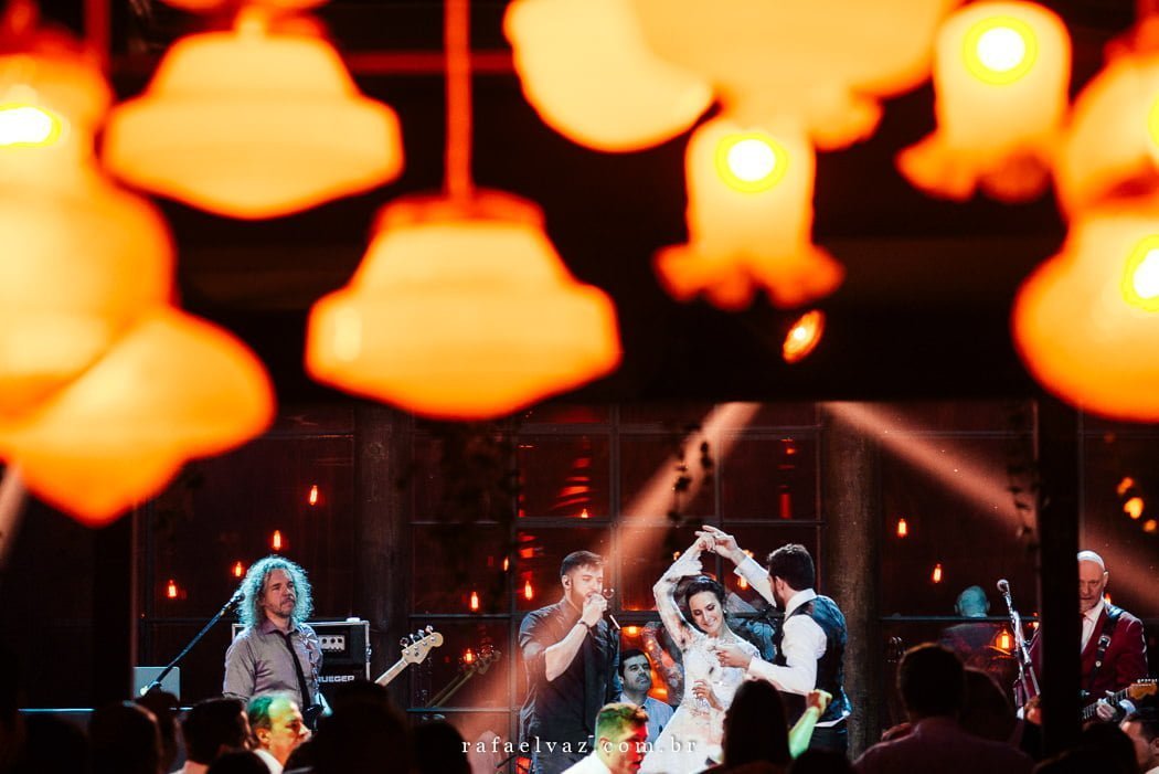 Noivos dançando no palco com a banda e várias luzinhas 